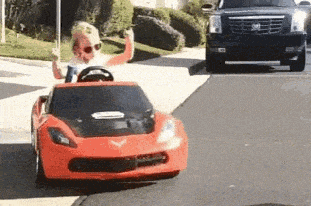 cool kid wearing sunglasses in a toy car with hands up
